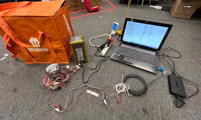 The physical thermal test rig — model with temperature sensors, laptop, power monitor, and insulated bag